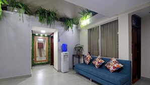 Una sala de estar con un sofá azul, cojines decorativos, un dispensador de agua y plantas colgantes.