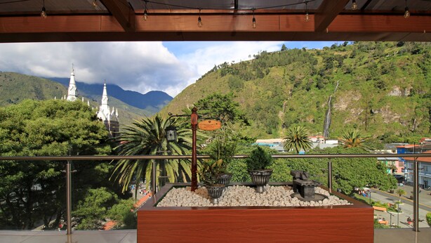 Un balcón con vista a una iglesia blanca, abundante vegetación y un paisaje montañoso.
