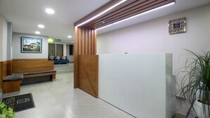 Un área de recepción con un banco de madera, un mostrador blanco, una planta en maceta y un cuadro en la pared.