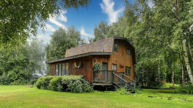 En træhytte med skrå tag, store vinduer og en trappe op til en terrasse.