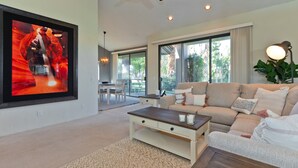 Una sala de estar moderna con un televisor de pantalla plana grande, un sofá color beige, una mesa de centro de madera y un ventanal con vistas al exterior.