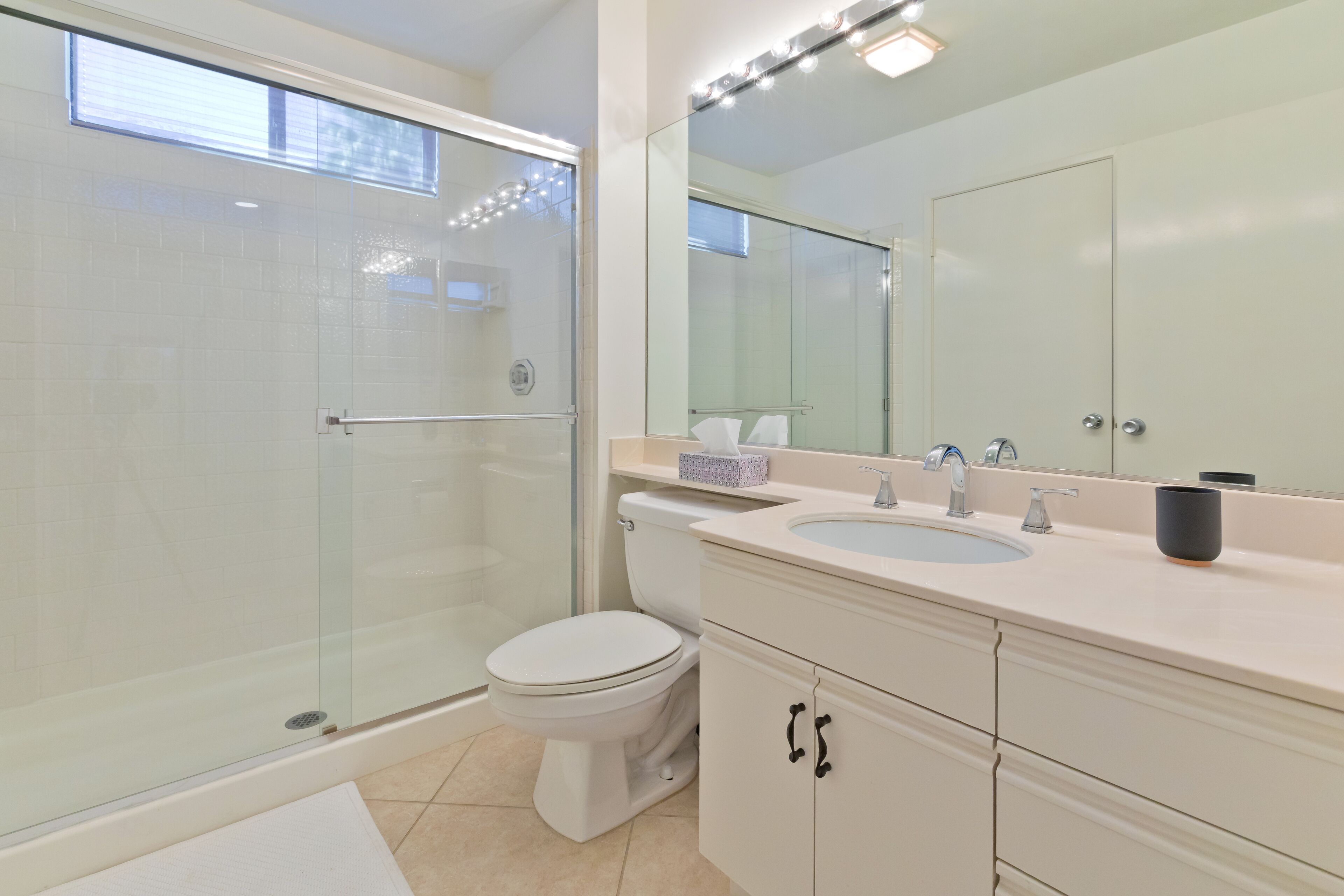 Une salle de bain moderne avec une douche à parois de verre, des toilettes blanches, un lavabo avec un miroir au-dessus et des meubles de couleur beige.