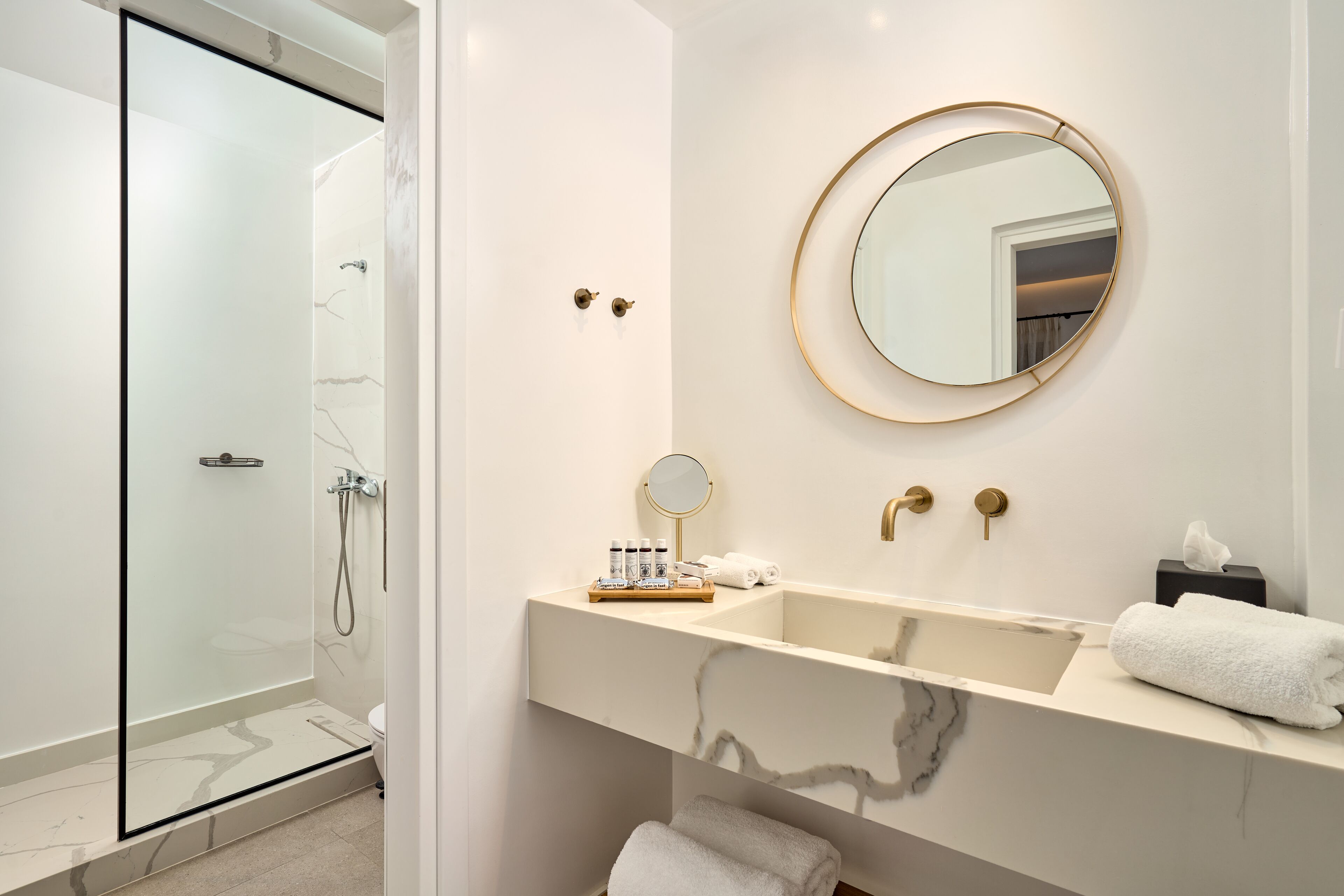 A modern bathroom with a glass shower enclosure, a marble vanity with a sink, and a round mirror.