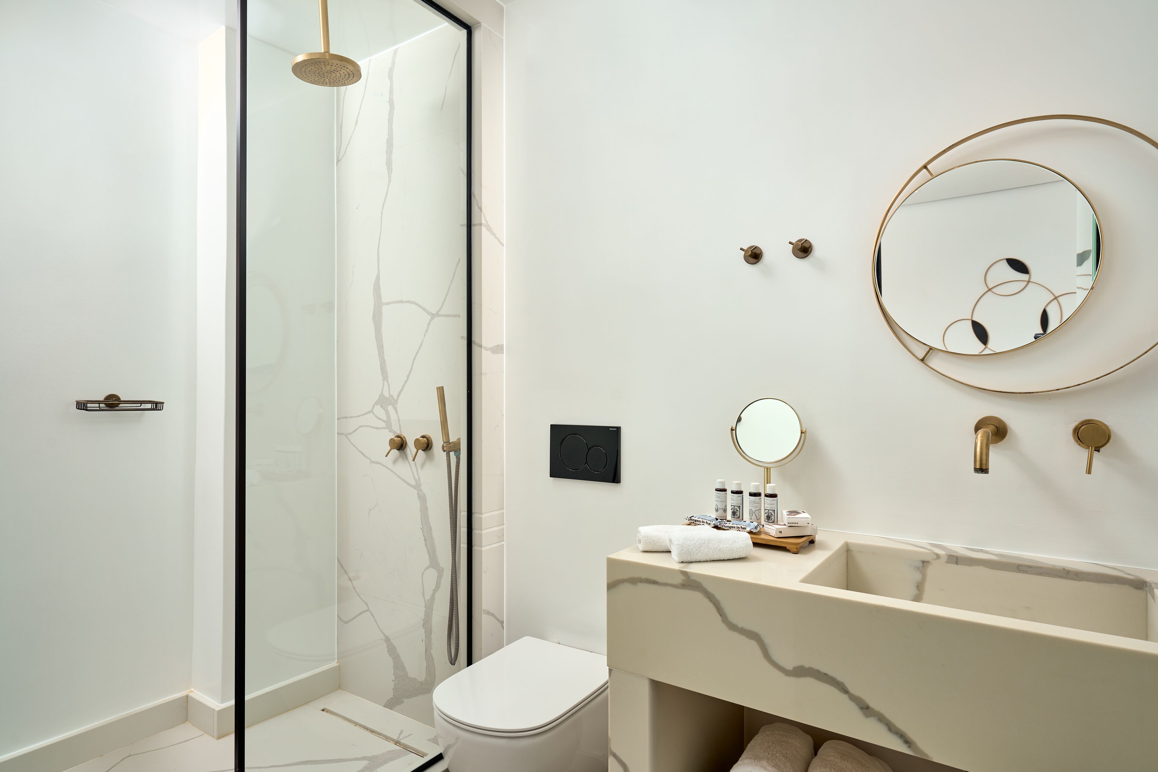 A modern bathroom with a glass-enclosed shower, a marble vanity, and a round mirror.