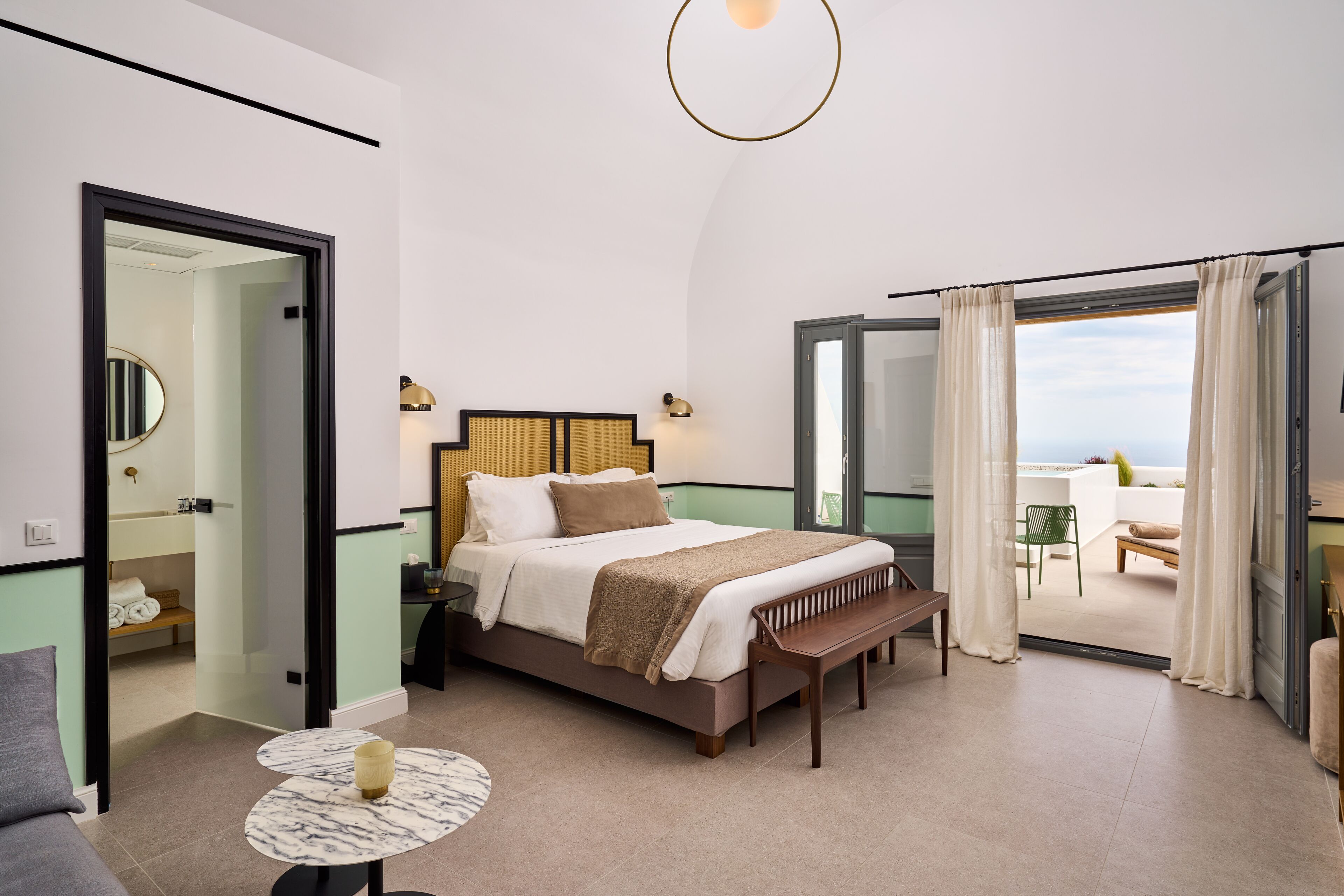 Un dormitorio con cama, mesita de noche, banco y vistas al exterior.
