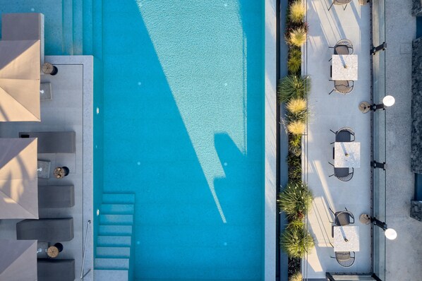 An aerial view of a swimming pool with surrounding outdoor seating and steps leading to a covered area. - Alleys All-Suite Hotel & Spa (Santorini)