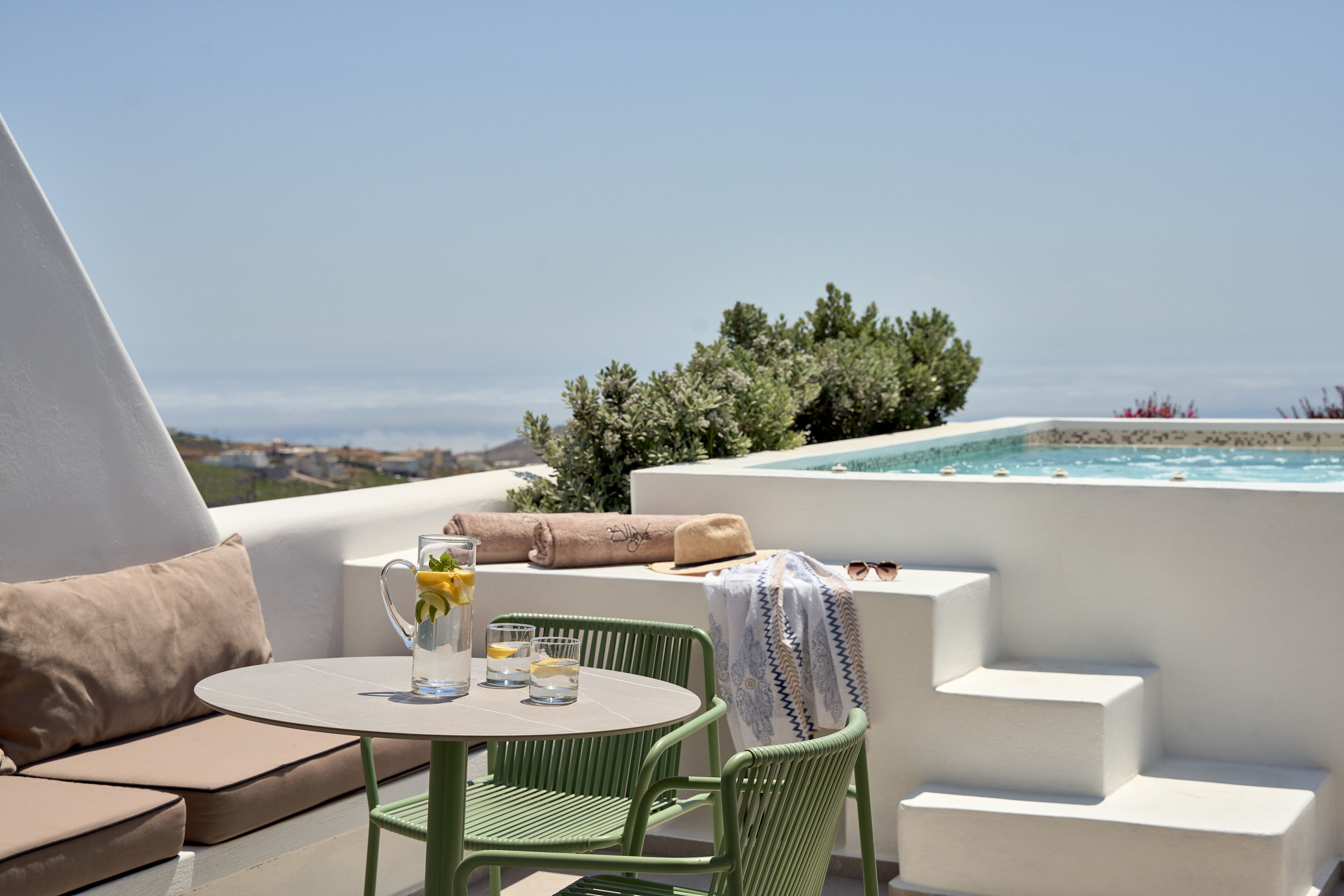 A terrace with a round table, green chairs, a sofa, and a hot tub.