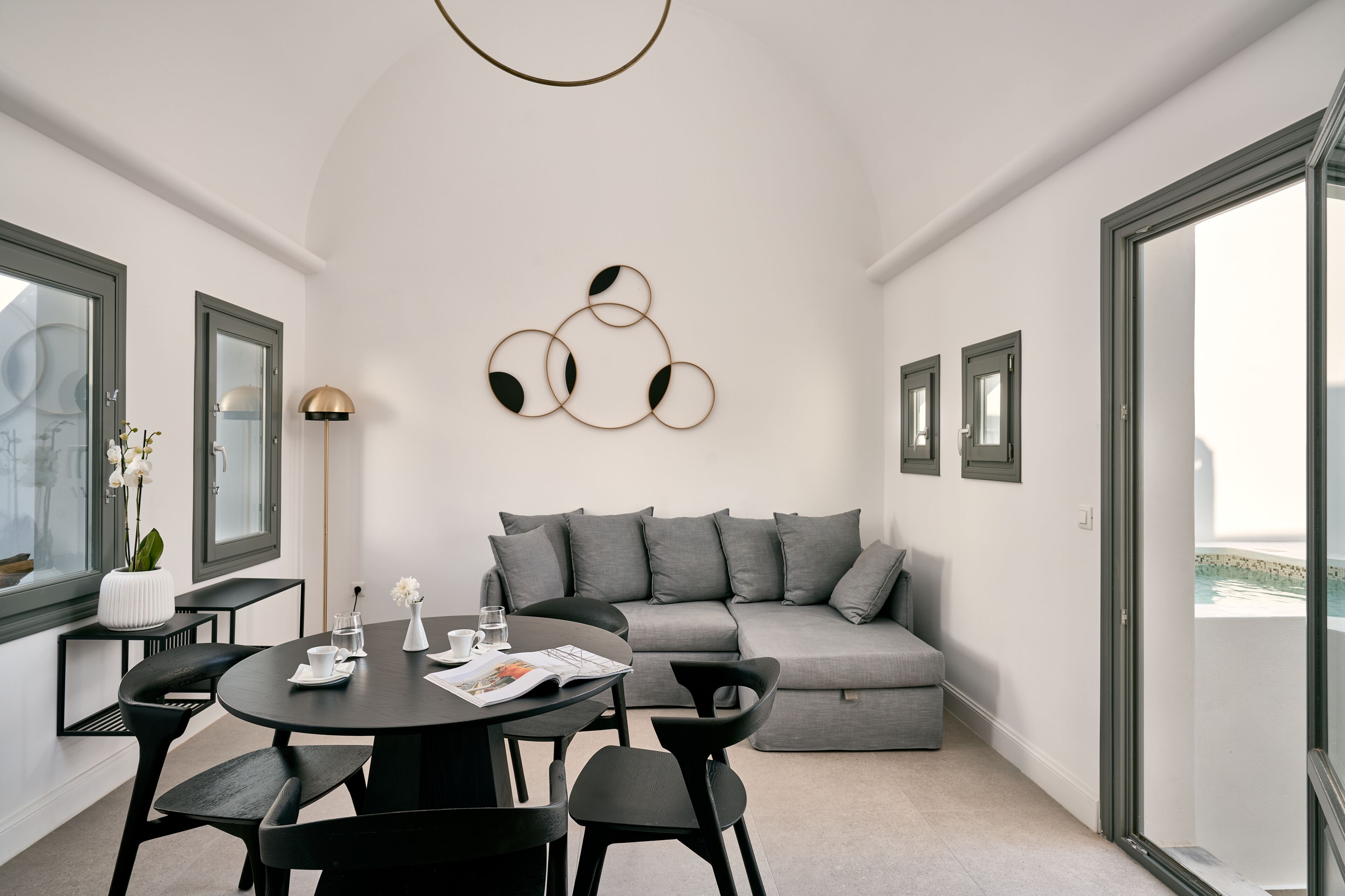 A modern living room with a grey sofa, black chairs, a round table with a magazine, and a wall art piece.