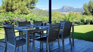 An outdoor patio with a table and chairs, surrounded by a wooden deck and a pergola. - La Gaude, villa 6 people-garden-pool-open view in a quiet (La Gaude)
