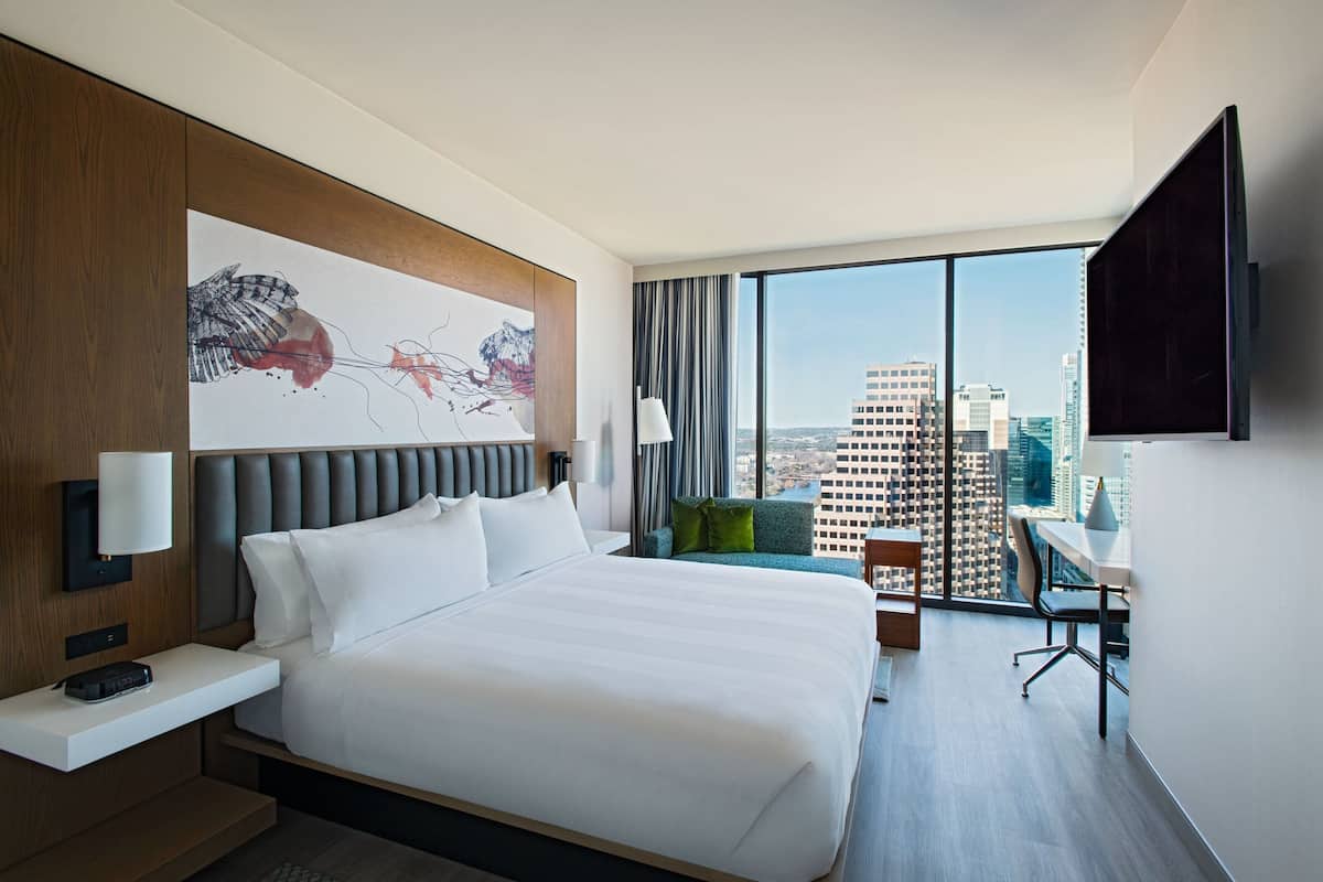 A modern hotel room with a large bed, a desk, and a view of the cityscape.
