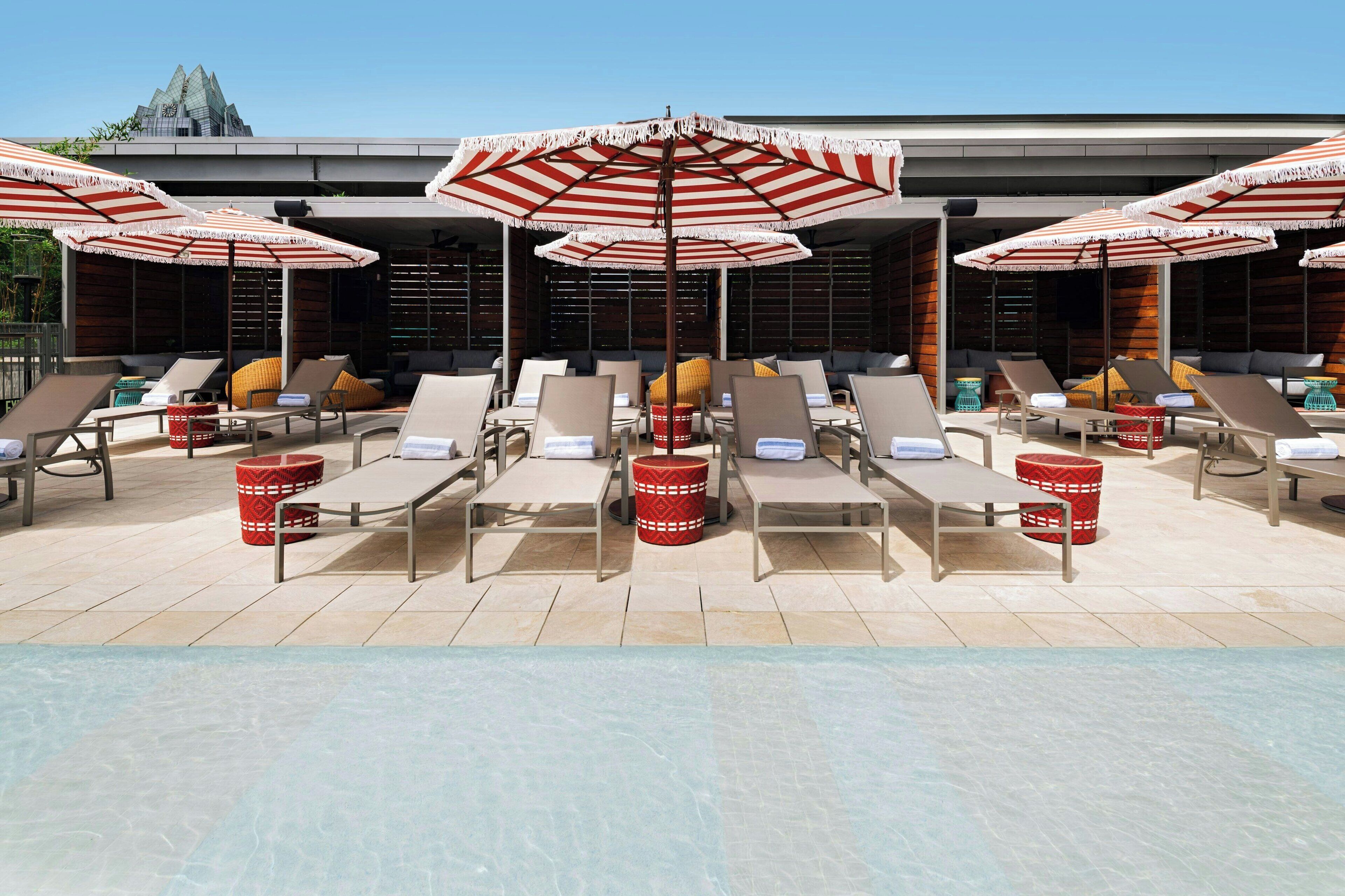 A poolside area with sun loungers, red patterned umbrellas, and red baskets.