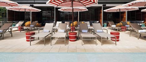 A poolside area with sun loungers, red patterned umbrellas, and red baskets.