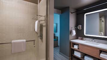 A modern bathroom with a glass shower enclosure, a vanity with a large mirror, and neatly folded towels.