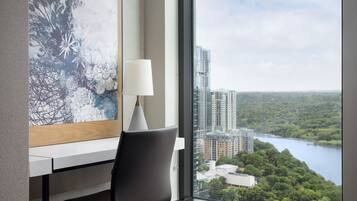 Habitación de hotel moderna con escritorio, silla y un amplio ventanal que ofrece vistas a la ciudad y a un lago.