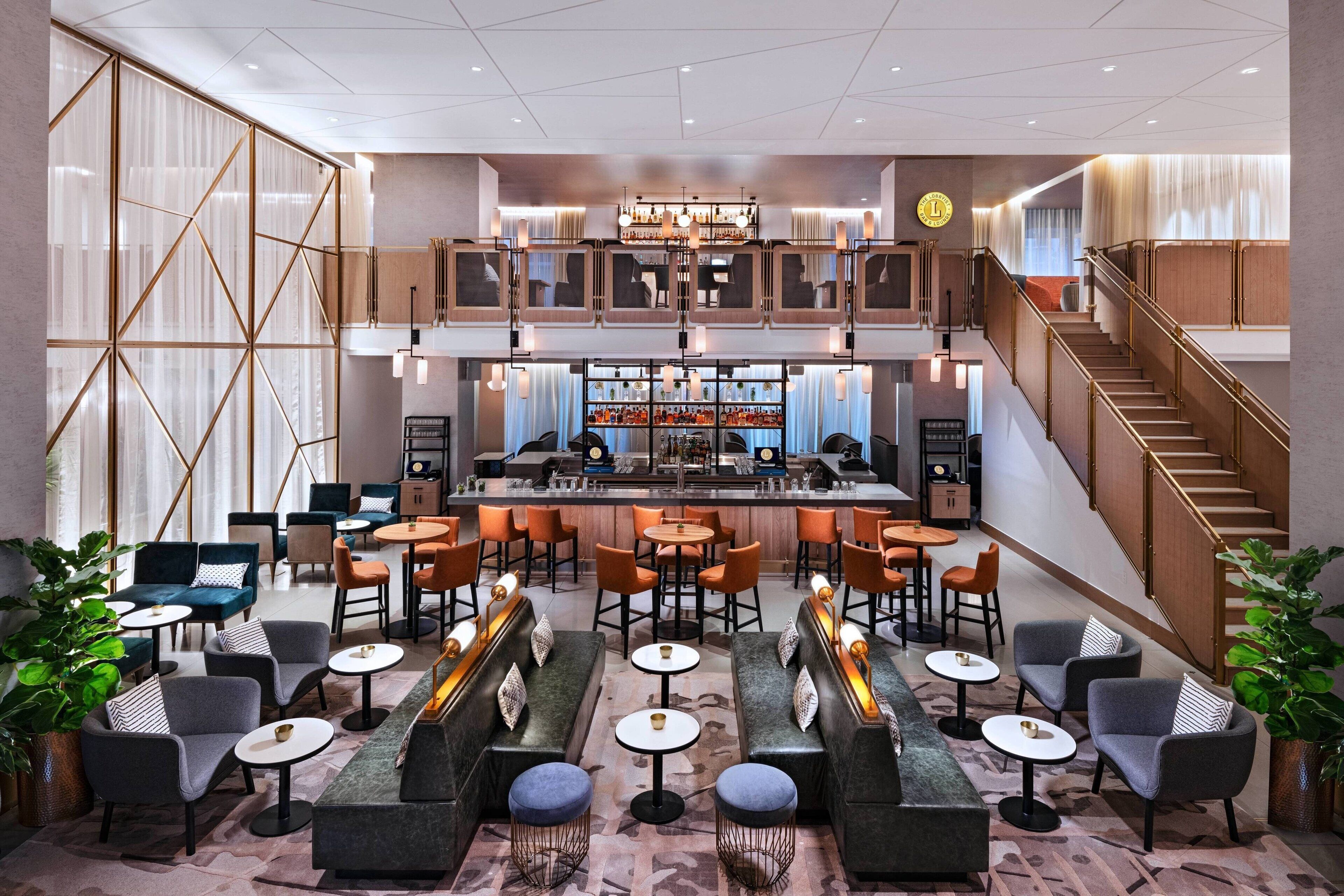 A modern hotel lobby with a bar area, seating arrangements, and a staircase.