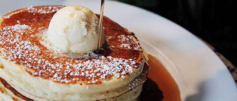 Une pile de crêpes arrosées de sirop, surmontée d’une boule de glace, le tout présenté sur une assiette blanche.
