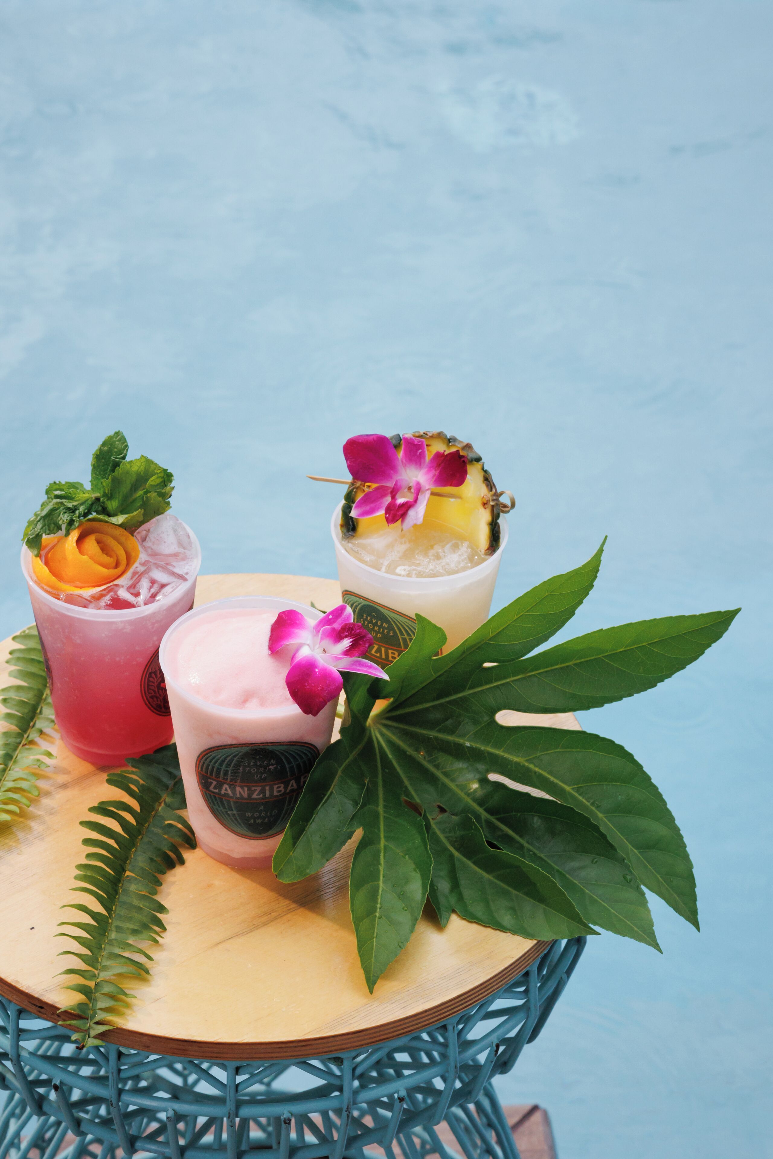 Three drinks on a wooden tray with a tropical plant.
