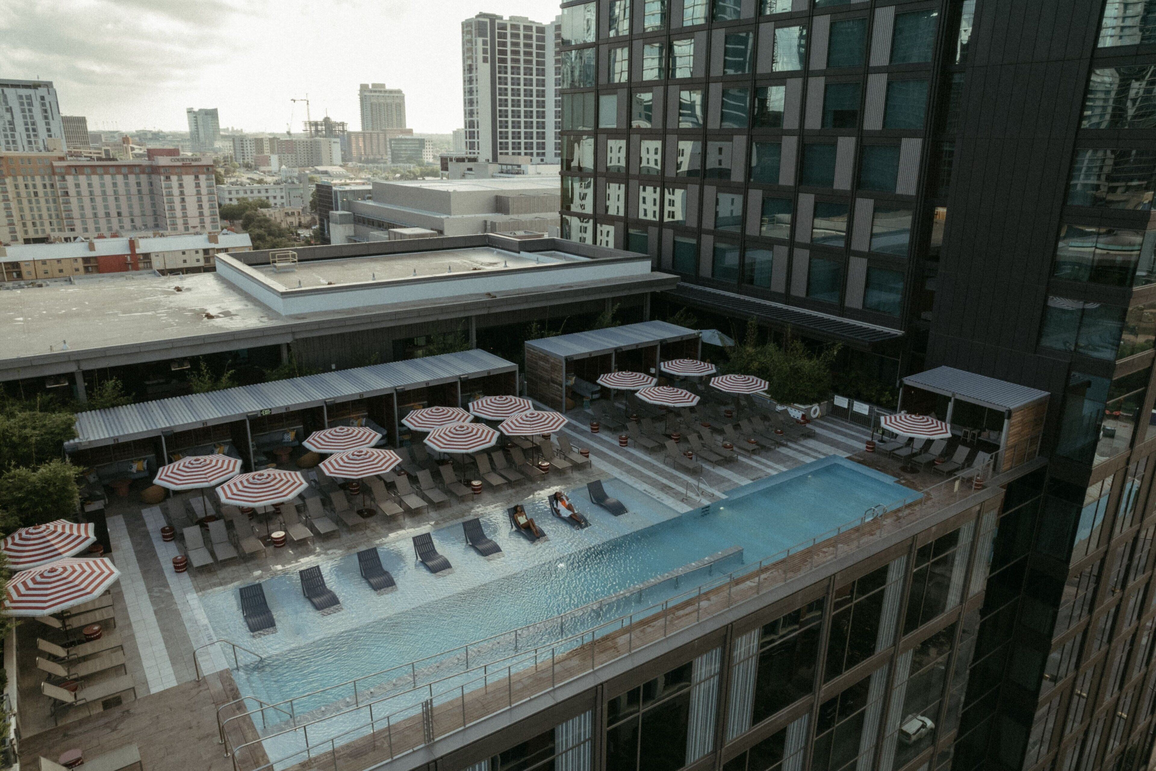 A rooftop pool with lounge chairs and umbrellas, surrounded by modern buildings.