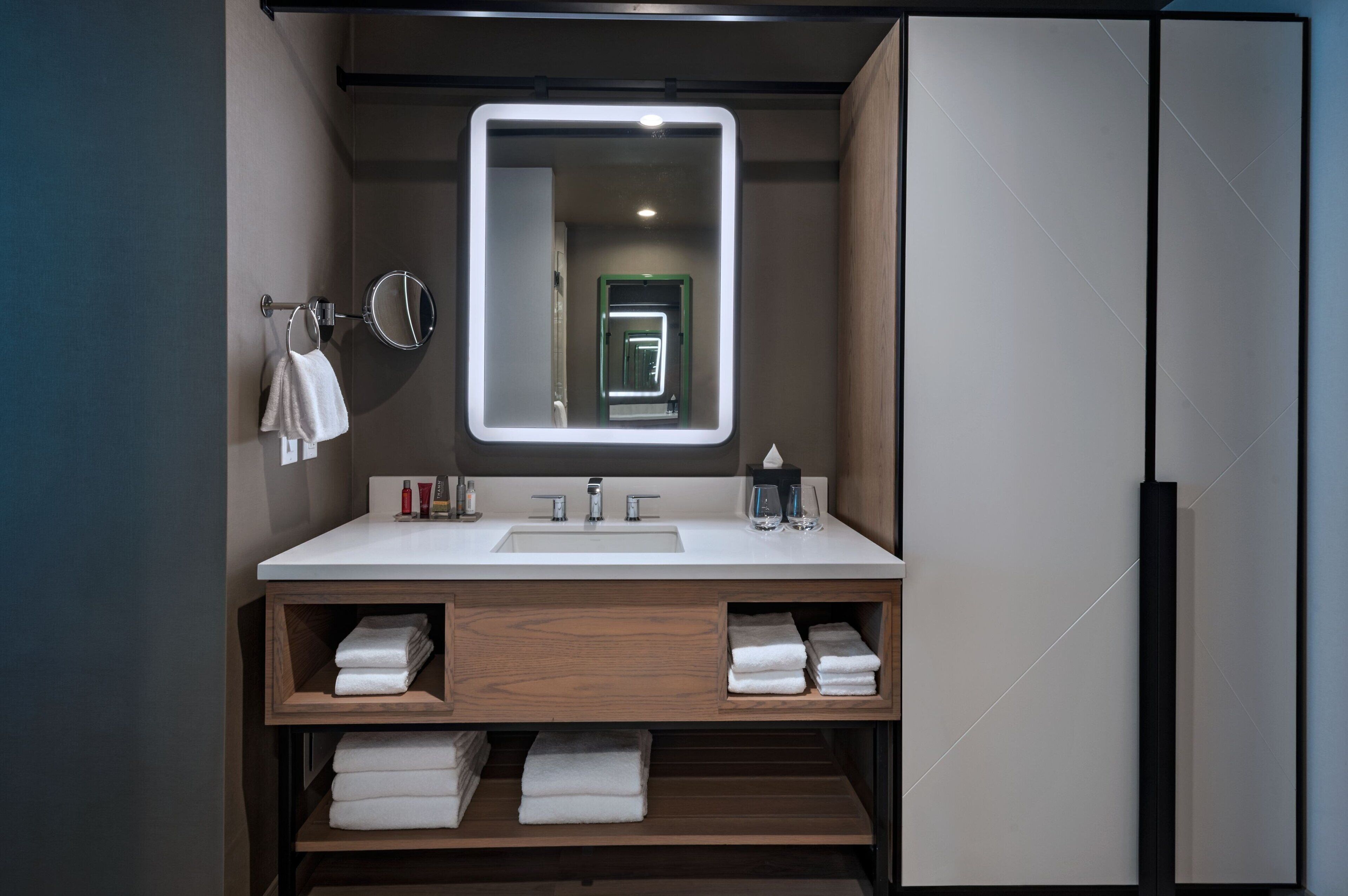 Un baño moderno con un espejo grande, lavabo blanco y repisas de madera para toallas.