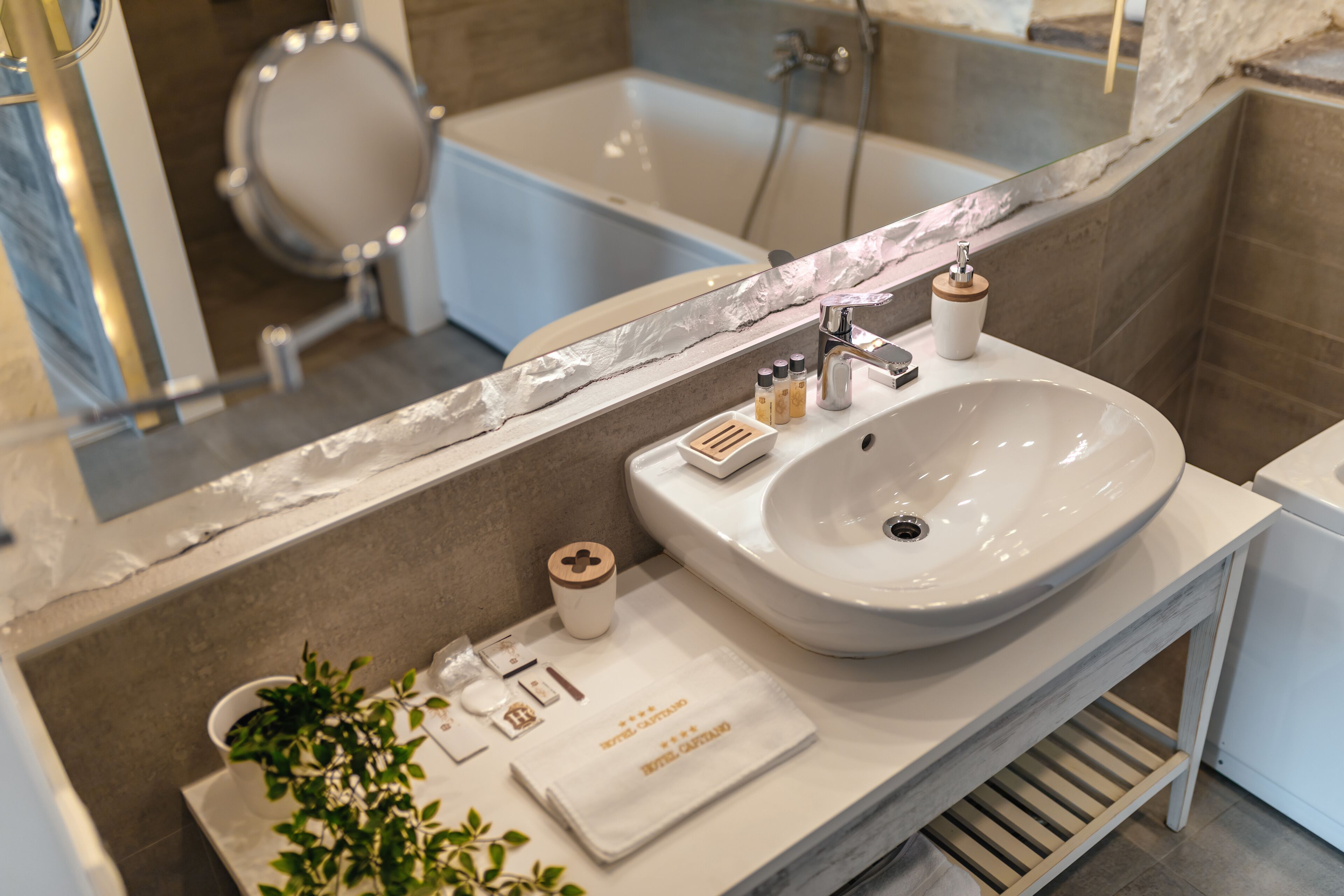 Ein modernes Badezimmer mit einem großen weißen Waschbecken, einem Spiegel mit Marmorablagen, einer Handbrause und einer Badewanne.