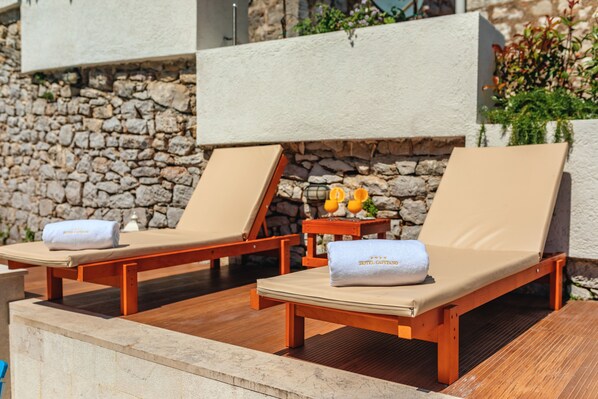 Dos sillones de madera con cojines color crema, una pared de piedra y una mesita con una toalla y una botella.
