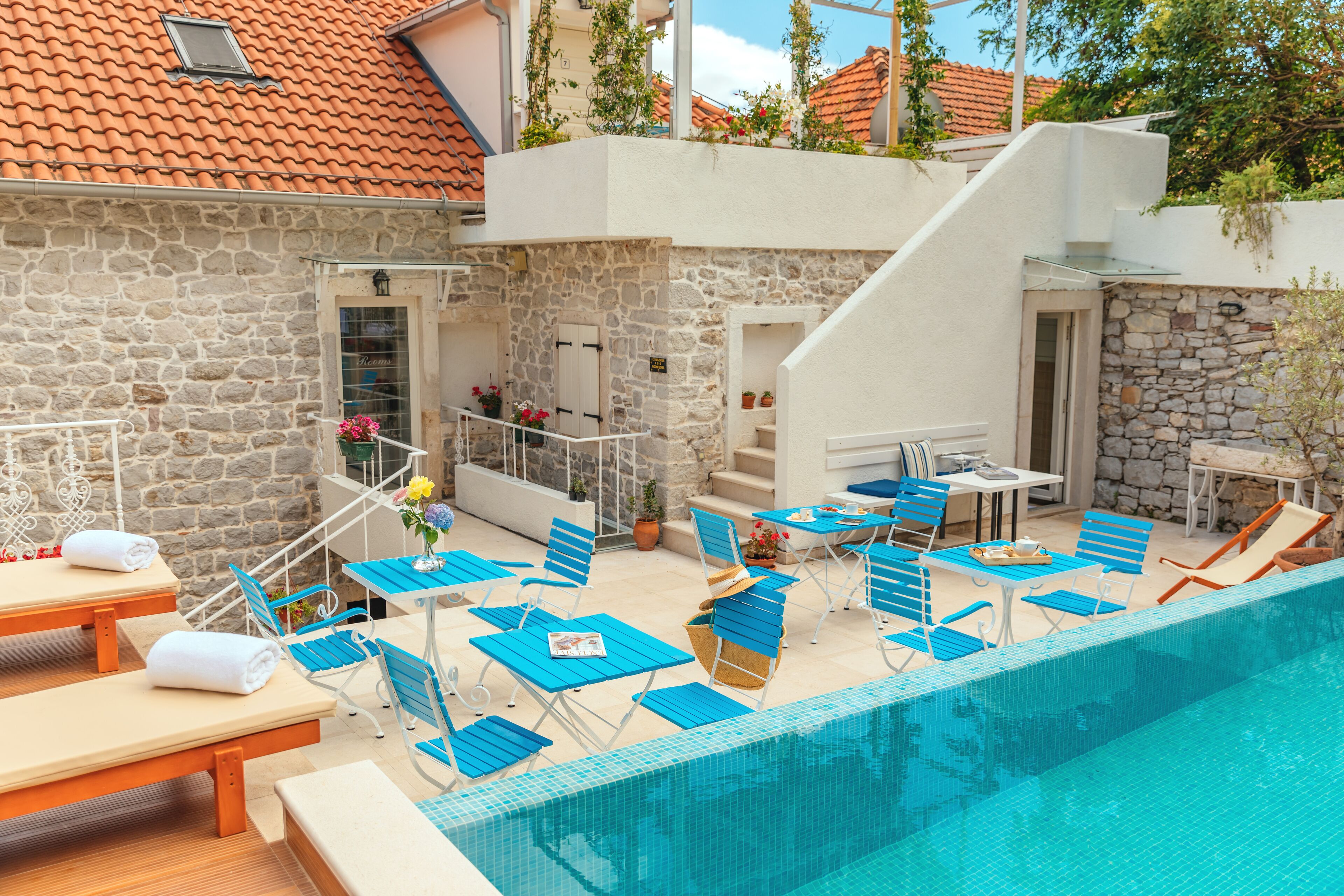 Área junto à piscina com paredes de pedra, cadeiras de descanso azuis e uma mesinha com bandeja.