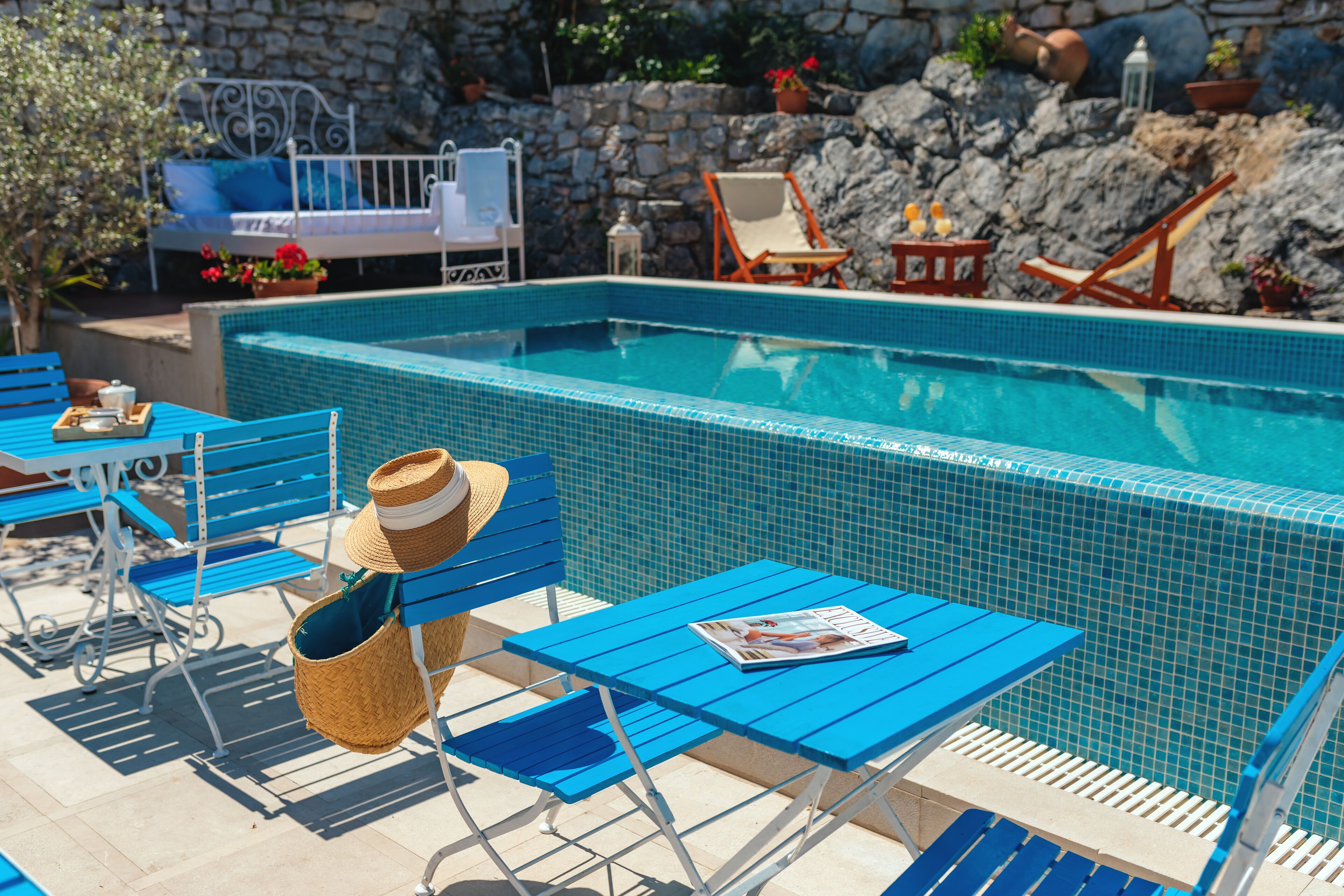 Un área de piscina con sillas reclinables azules, una cesta de mimbre y una revista sobre una mesa.