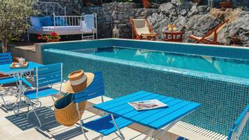 Un área de piscina con sillas reclinables azules, una cesta de mimbre y una revista sobre una mesa.