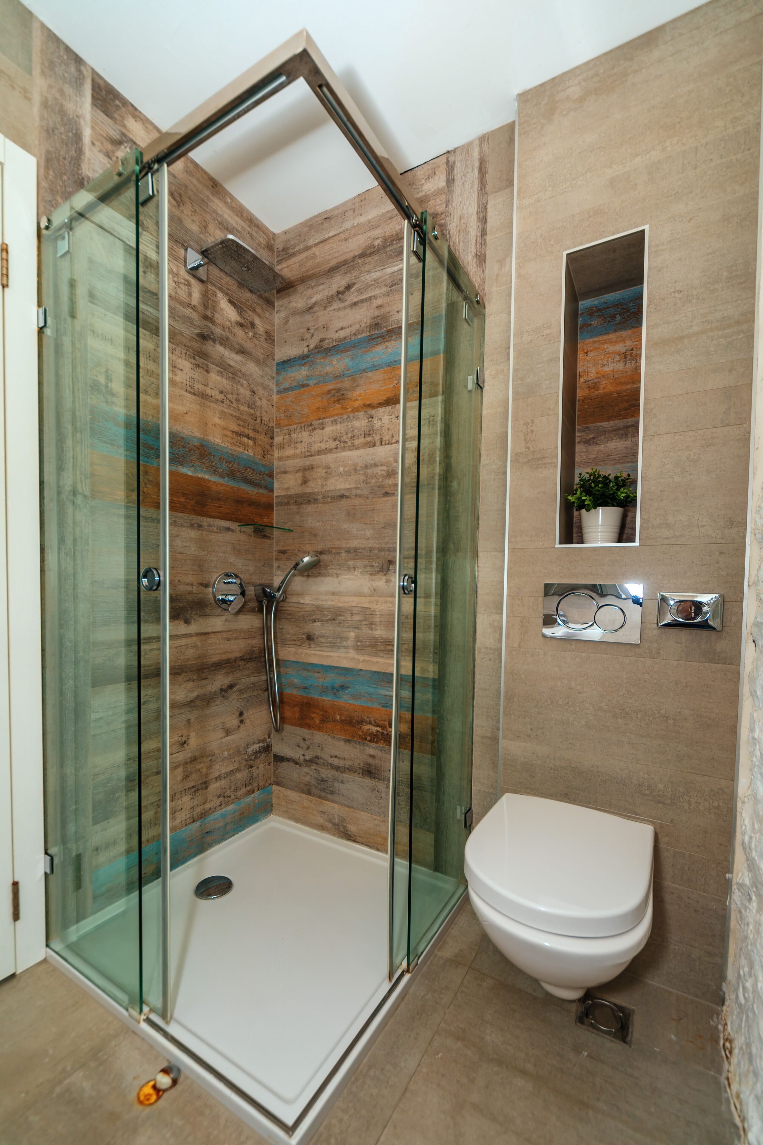 Een moderne badkamer met een douchecabine van glas, een wit toilet en een klein plankje met een plant.