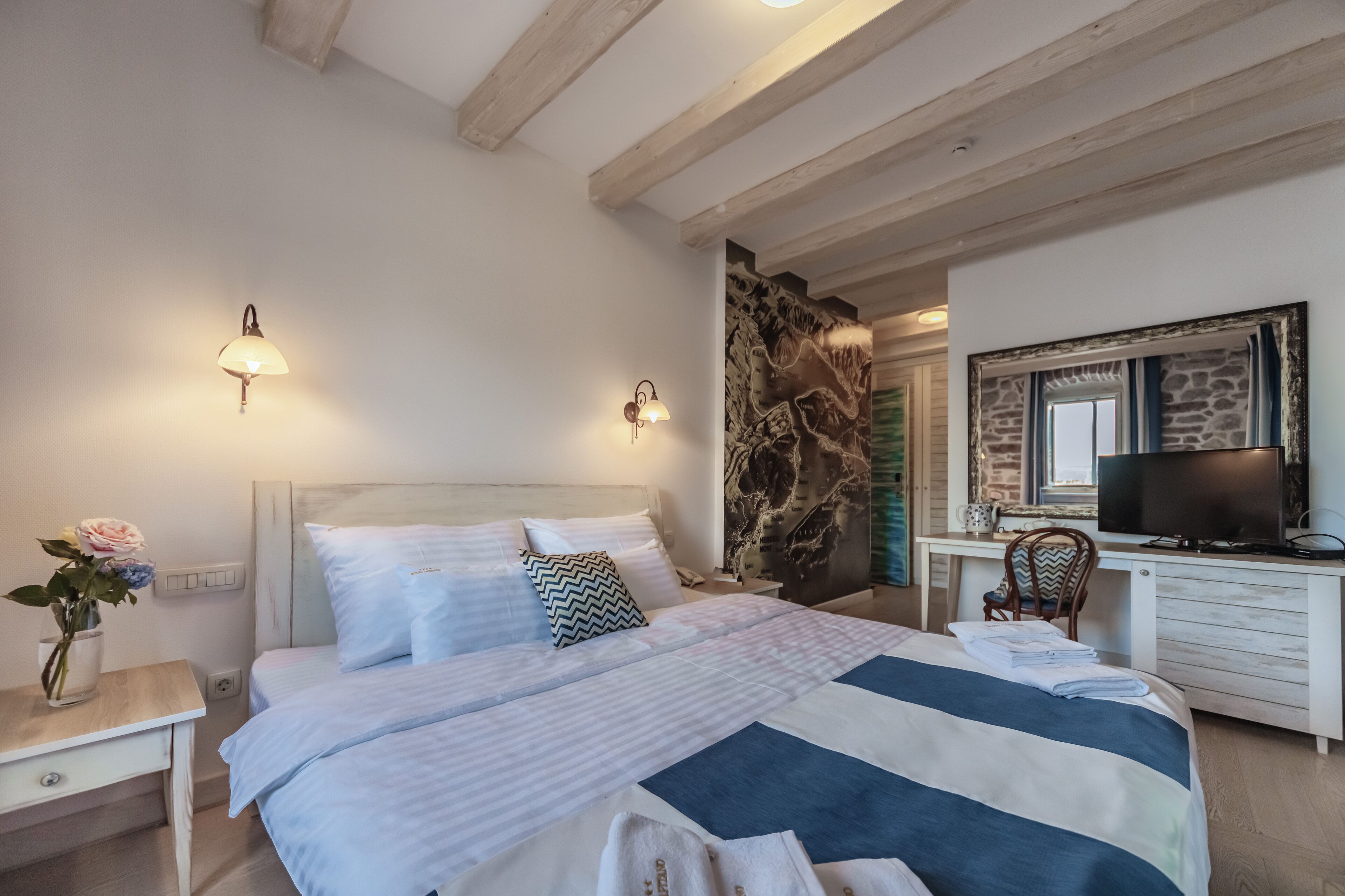 Un dormitorio con cama, mesita de noche, lámpara y televisor sobre un escritorio.