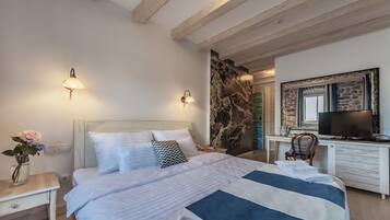Un dormitorio con cama, mesita de noche, lámpara y televisor sobre un escritorio.