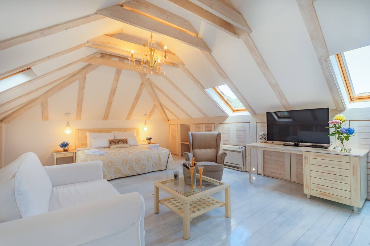 A spacious loft bedroom with a large bed, a sitting area with a sofa, a television, and a desk with a computer.