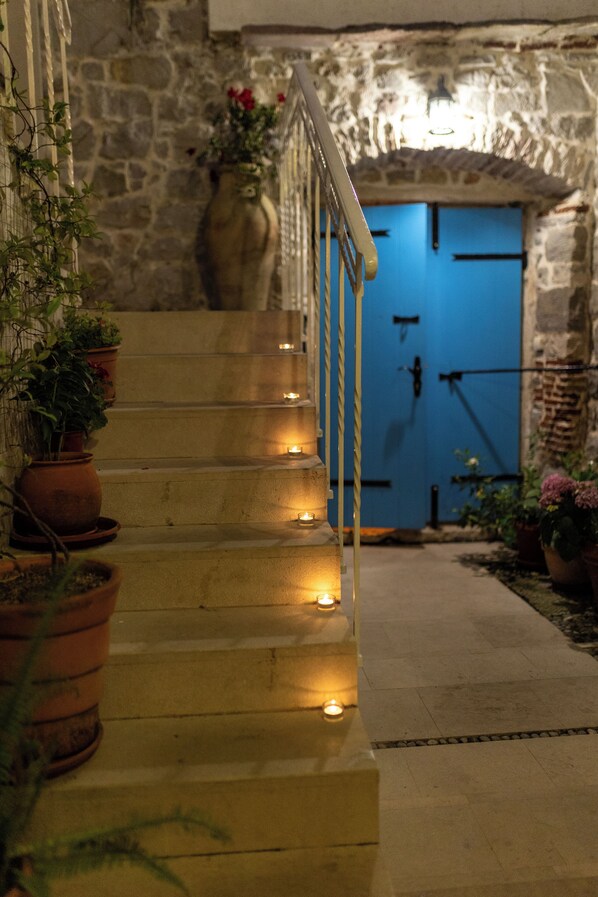 Una escalera de piedra que lleva a una puerta azul, con macetas a la izquierda y velas a lo largo de los escalones.
