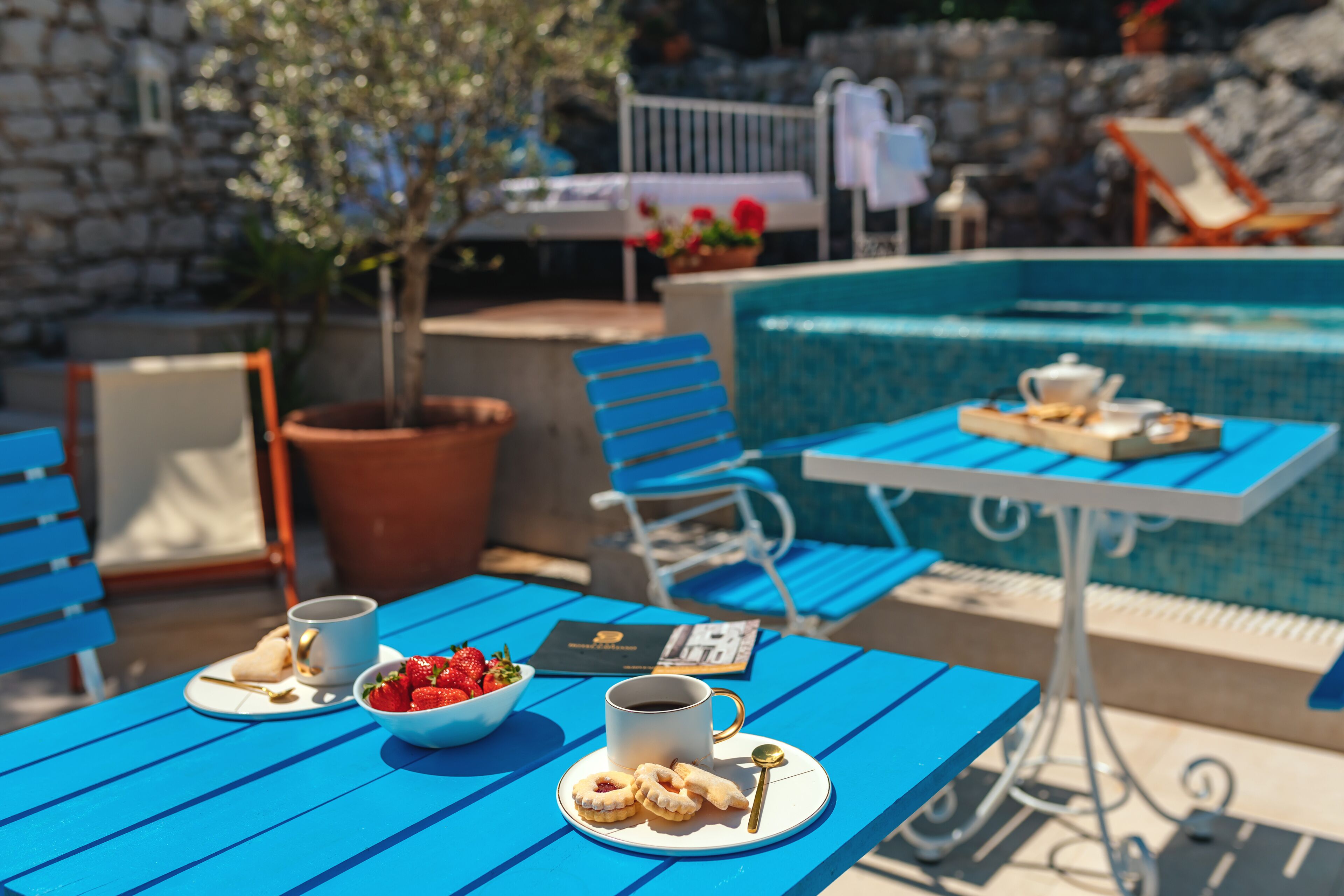 Een zwembadgedeelte met blauwe tafels, stoelen en een eethoek met borden vol aardbeien en koekjes.