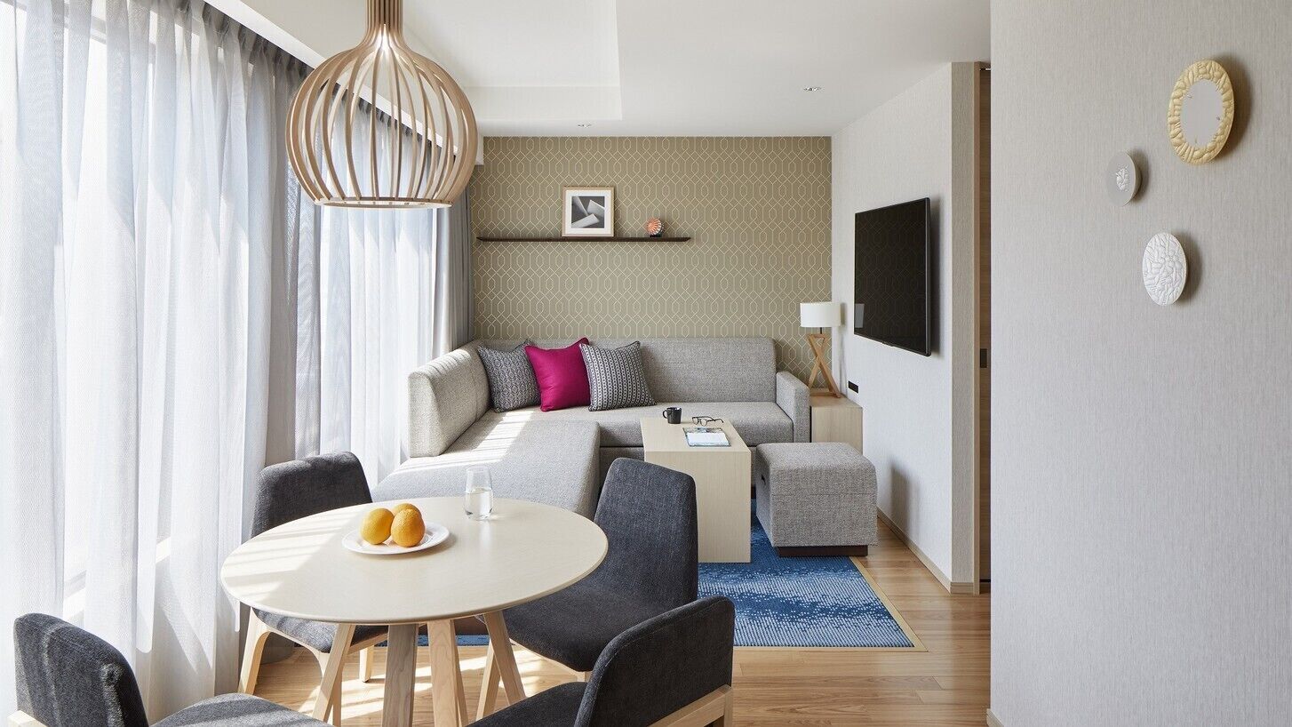 Un salon moderne avec un canapé, un téléviseur, une table à manger avec des chaises et un mur décoré de motifs.