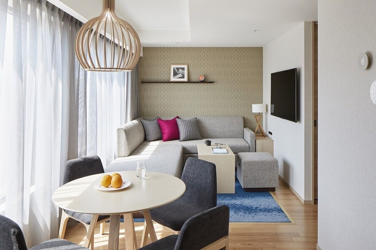 A modern living room with a sofa, a TV, a dining table with chairs, and a patterned wall.