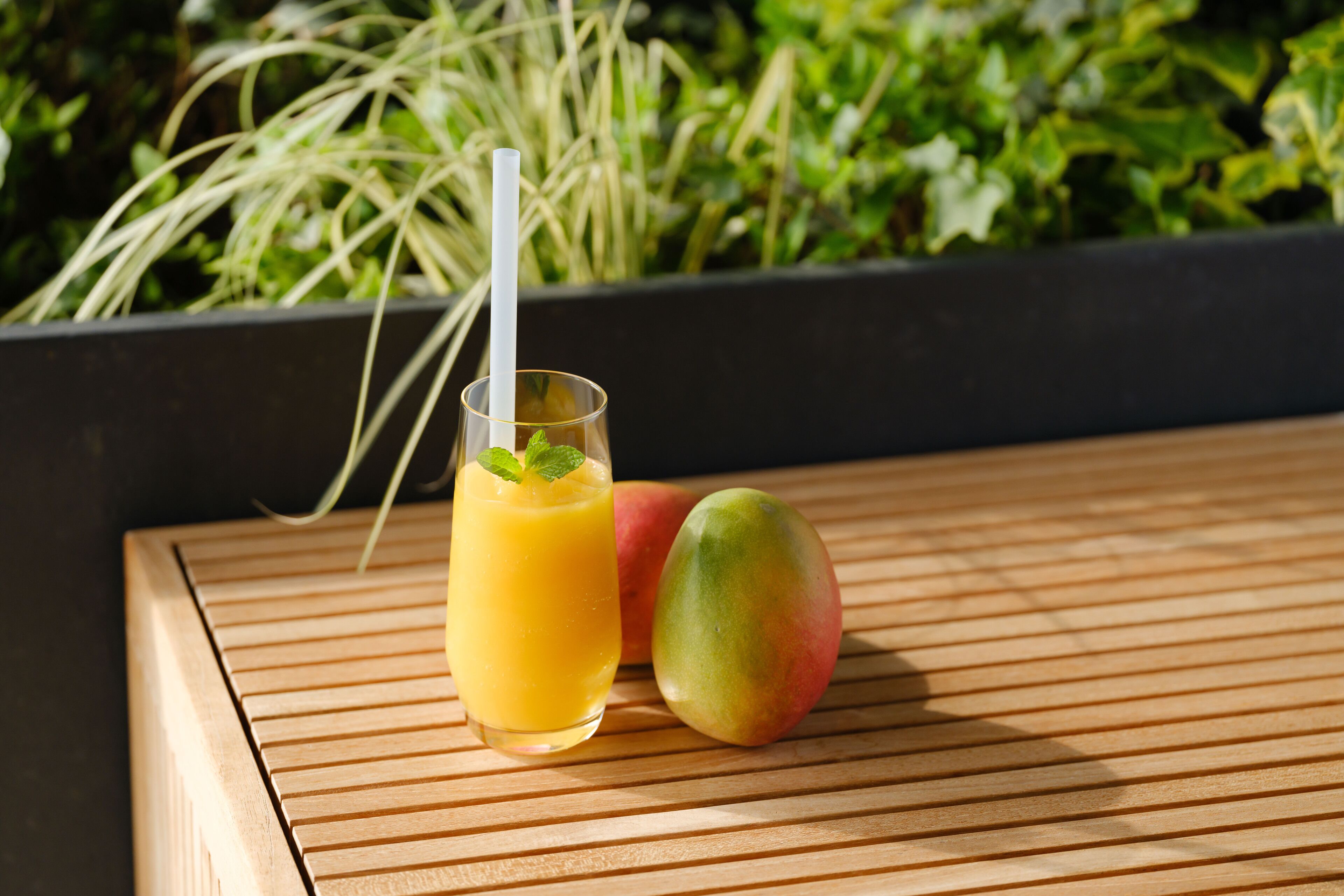 A glass of orange juice with a straw and a mango on a wooden surface.