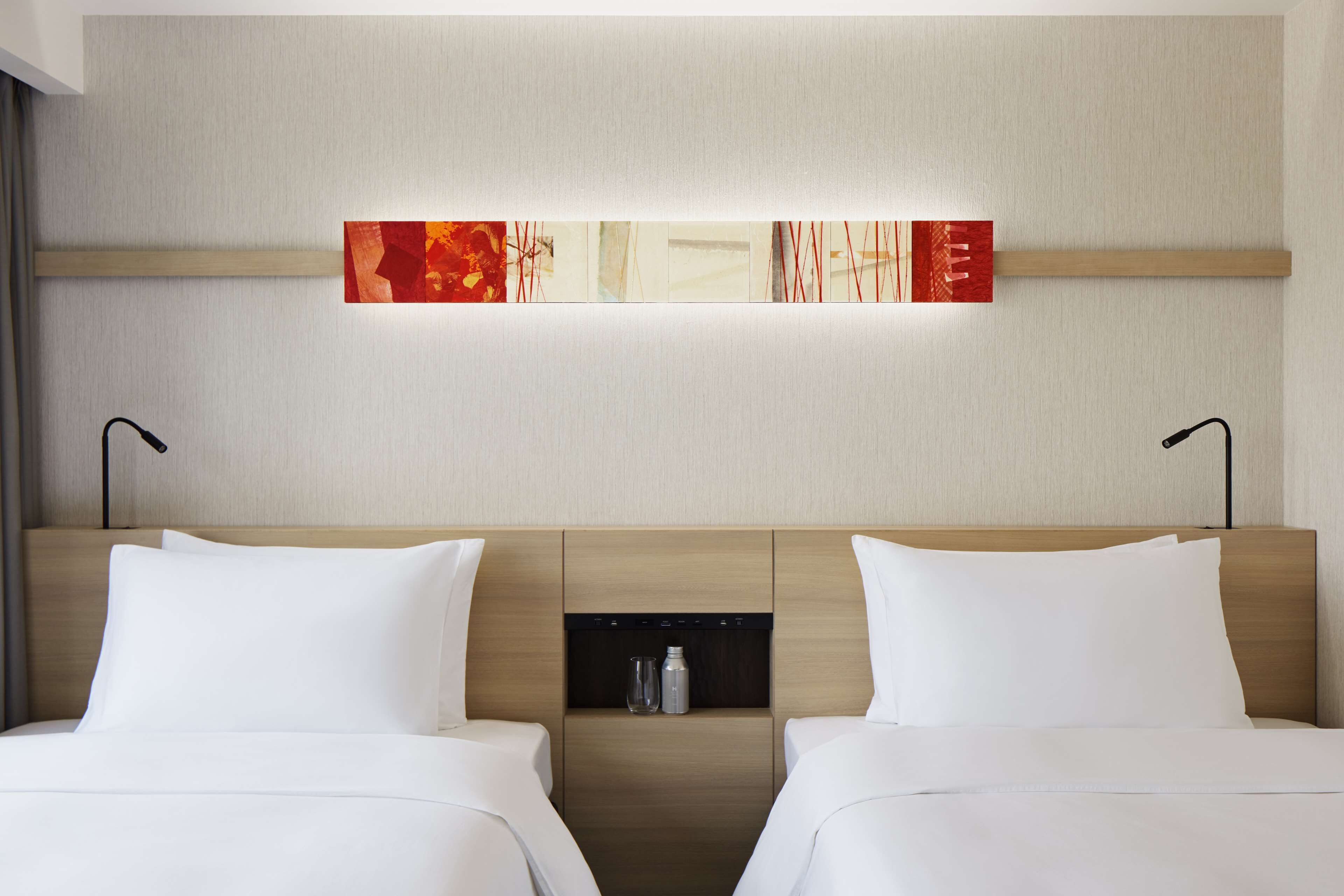 Habitación de hotel con dos camas, cabecero de madera, minibar y una obra de arte colgada en la pared.