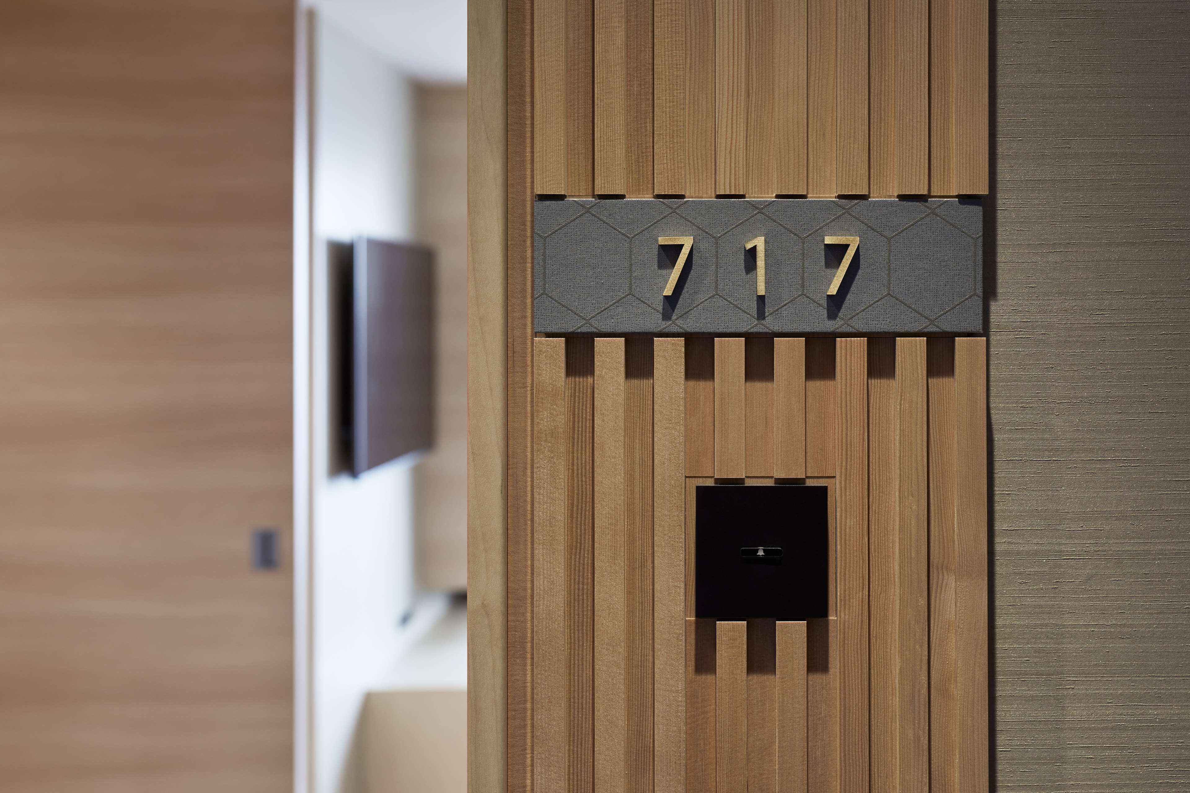 A wooden wall with a number plaque reading "717" and a small black square object below it.