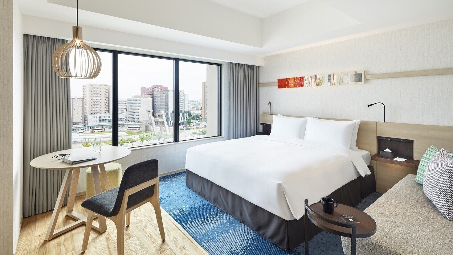 Une chambre d’hôtel avec un grand lit, un bureau avec une chaise, une petite table et une vue sur la ville.