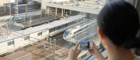 A person taking a photo of a train station with multiple tracks and a modern architectural structure in the background.
