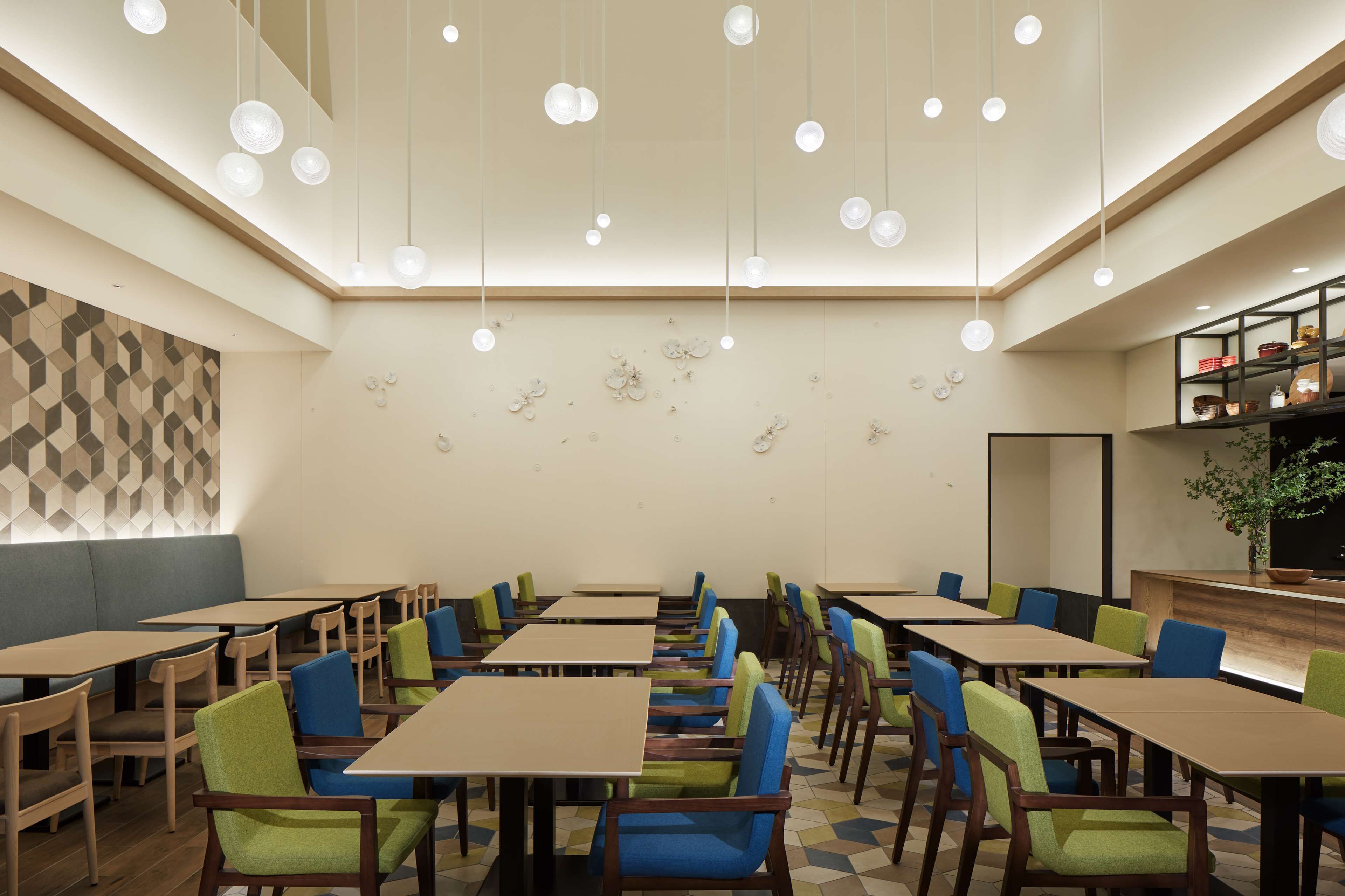 A modern dining area with multiple tables and chairs, a geometric patterned wall, and a wooden reception desk with a plant.