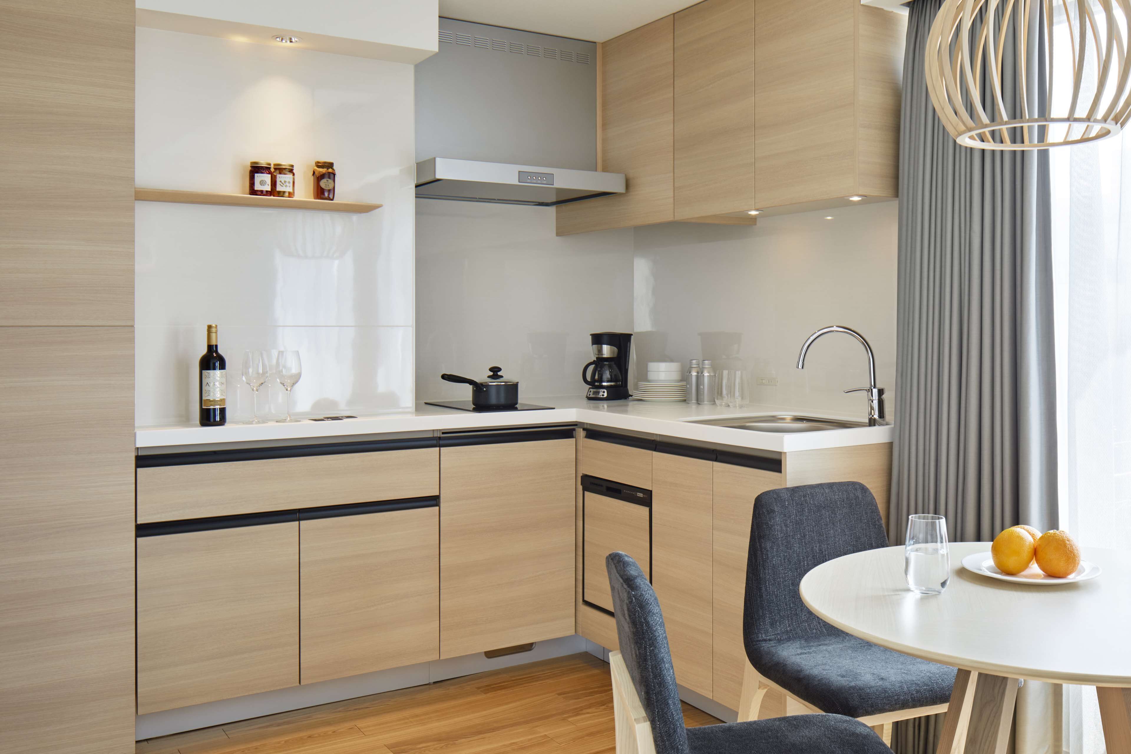 A modern kitchen with wooden cabinets, a white countertop, a built-in oven, and a dining area with a round table and chairs.