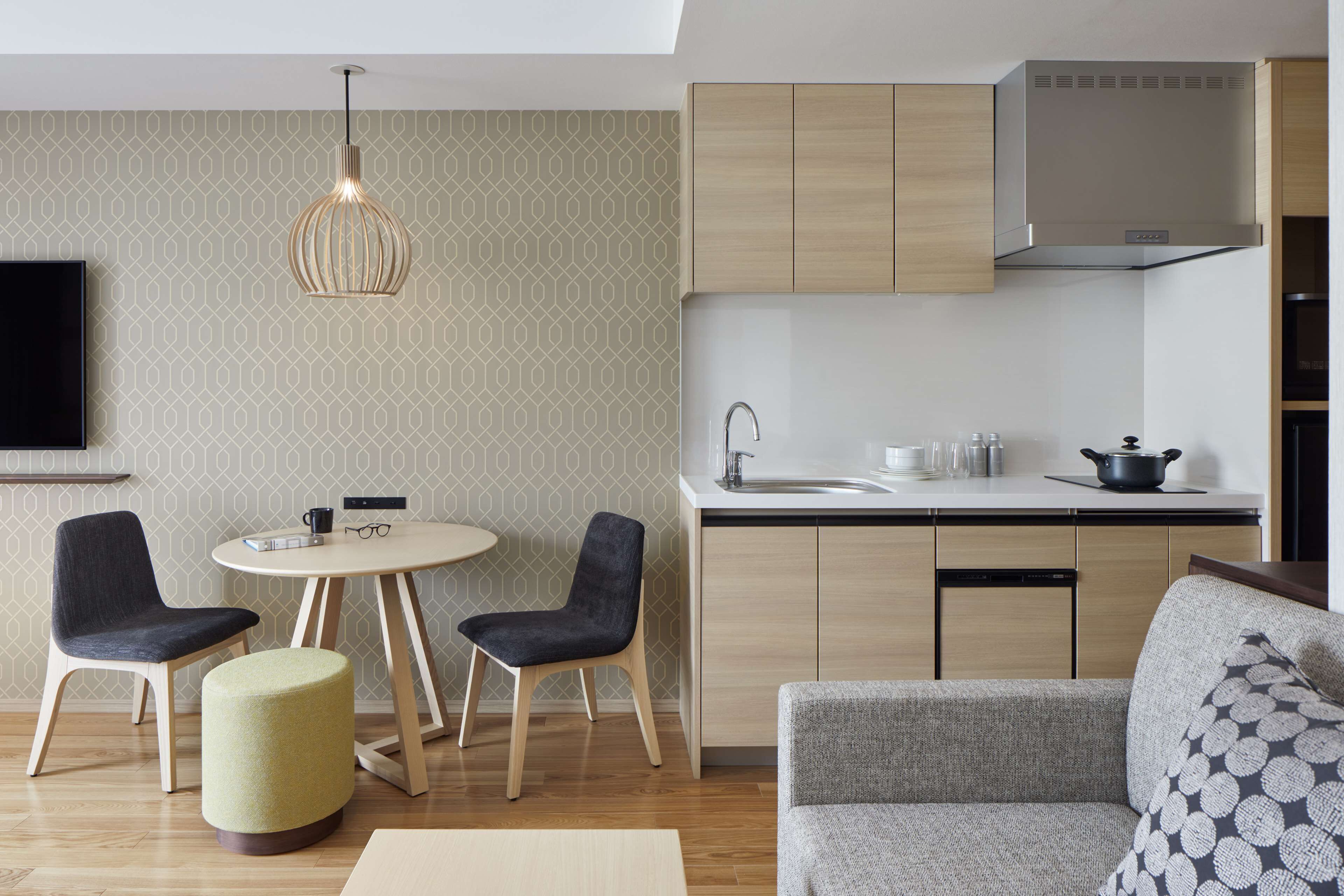 Una cocina moderna con armarios de madera, horno empotrado y un lavamanos. Hay una zona de comedor con dos sillas y una mesa, y un sofá en la sala de estar.