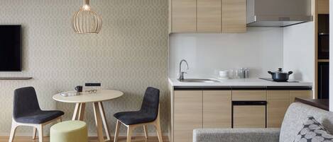 Una cocina moderna con armarios de madera, horno empotrado y un lavamanos. Hay una zona de comedor con dos sillas y una mesa, y un sofá en la sala de estar.