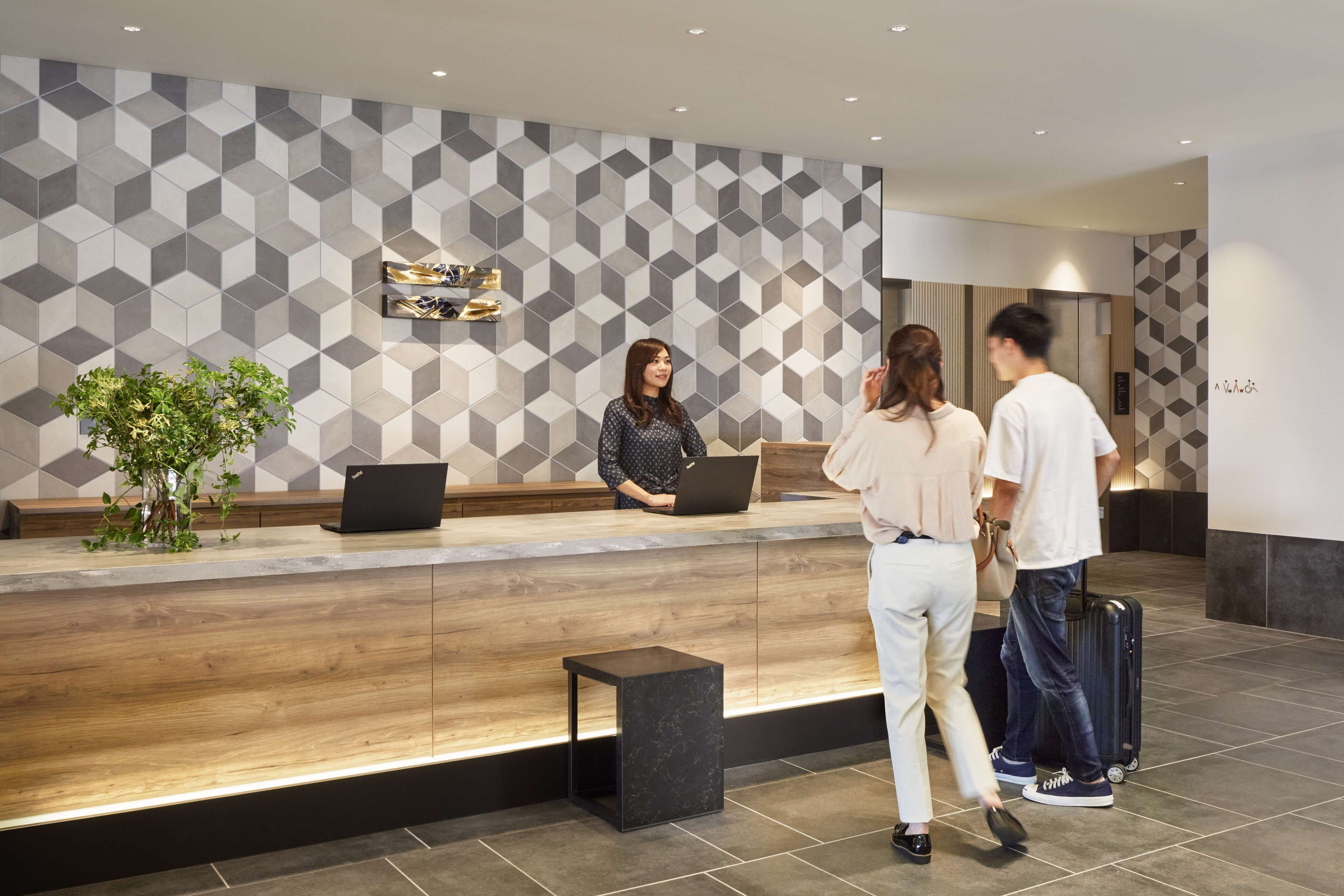 A reception desk with a geometric patterned wall, a laptop, and a plant.