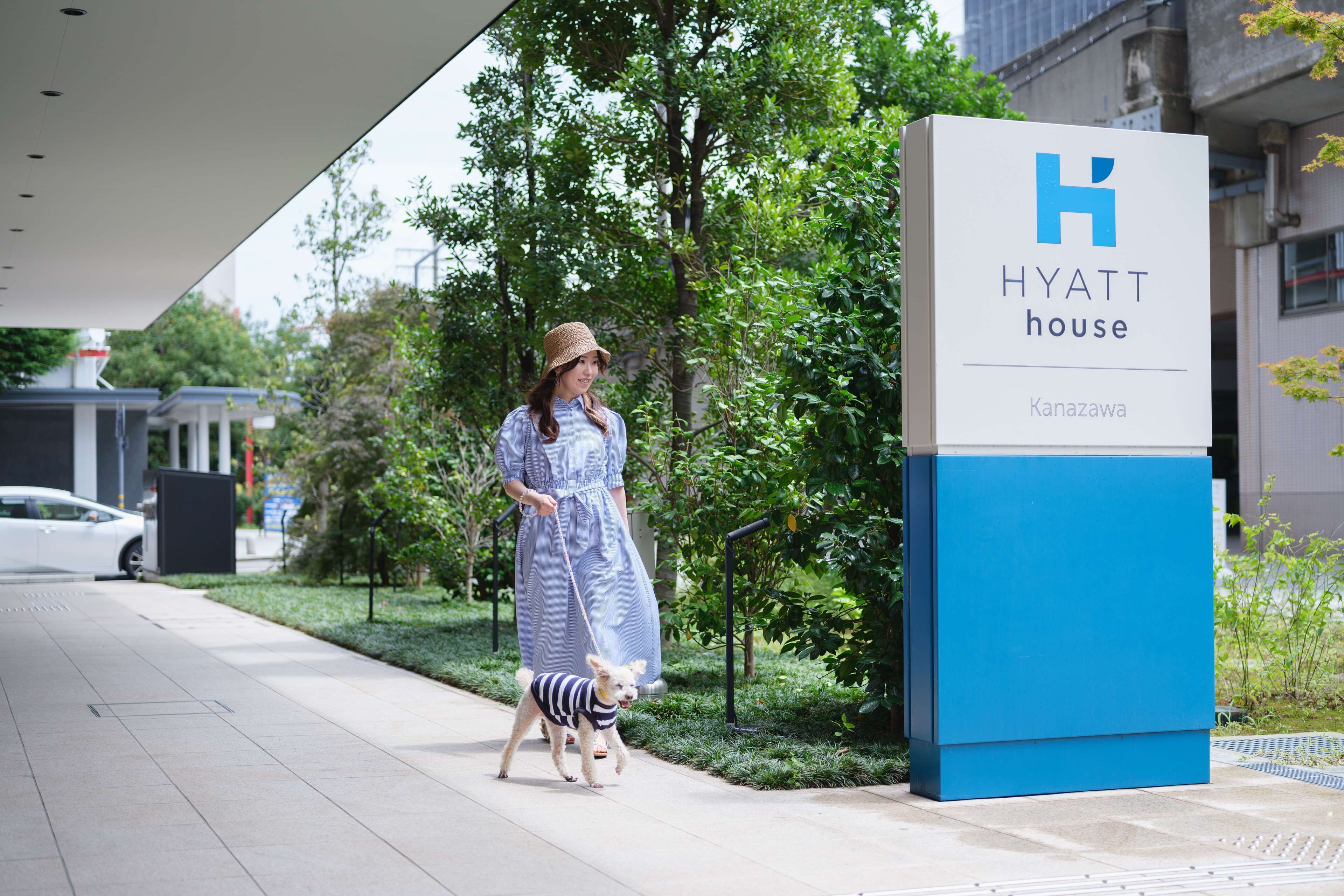 Une femme promène un chien devant l’enseigne d’un hôtel Hyatt House à Kanazawa.