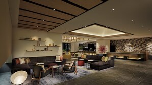 Ein modernes Wohnzimmer mit einem Ecksofa, Sesseln, einem Couchtisch und einem gemusterten Teppich. Im Hintergrund sind Regale mit Dekoration und eine Bar zu sehen.
