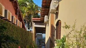 A narrow brick pathway flanked by lush greenery and potted plants, leading to a building with a tiled roof and a visible entrance.
