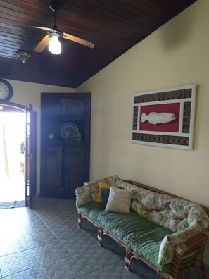 A room with a wooden ceiling, a ceiling fan, a clock, a wall-mounted fish decoration, a floral-patterned sofa, and a tiled floor.